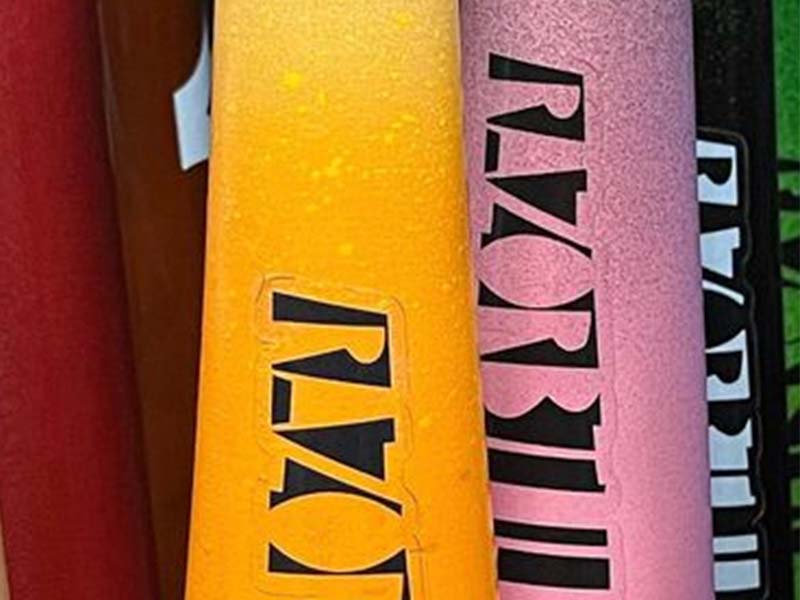 Yellow, red, and pink Razorbill maple wood bats lined up side by side, each featuring the signature Razorbill bat logo on the barrel.